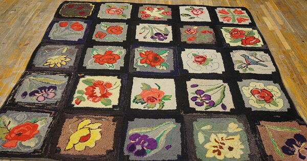 Hooked rug with a colorful grid pattern of various floral motifs resting on distressed wood flooring.