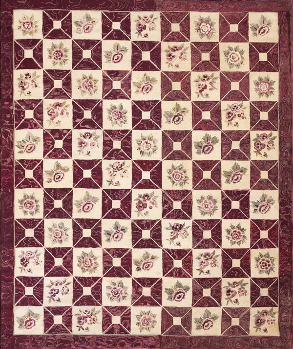 A textured rug in cream and deep maroon with a repeating geometric grid and small floral motifs.