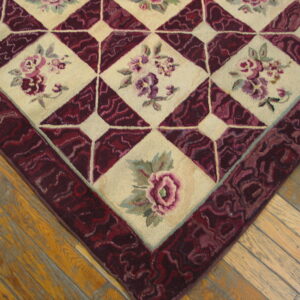 Close-up of a floral rug featuring cream diamond panels and a deep burgundy geometric border on wood floors.