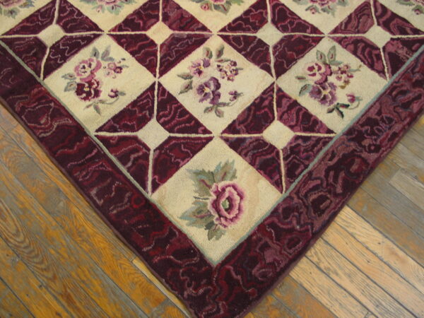 Close-up of a floral rug featuring cream diamond panels and a deep burgundy geometric border on wood floors.