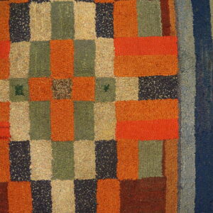 High-pile, multi-colored rug with checkerboard patterning and vertical stripes rests on wood flooring.