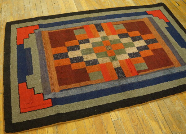 Geometric rug with multi-color blocks and concentric borders of orange, blue, and green on light wood planks.