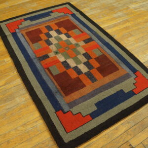 Geometric checkered rug with wide block borders in red, blue, green, and black on golden wood planks.