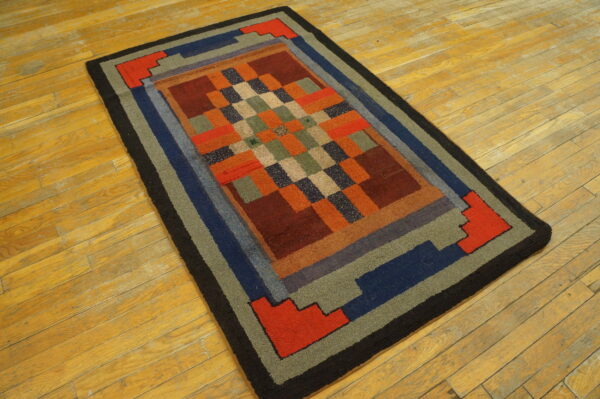 Geometric checkered rug with wide block borders in red, blue, green, and black on golden wood planks.