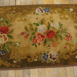 A plush runner rug with multicolored floral designs on an olive and brown ground, placed on wood floorboards.