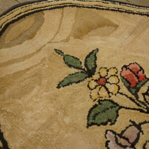 Detail of a tan hooked rug with a floral pattern of red, yellow, and green on rustic wood floor.