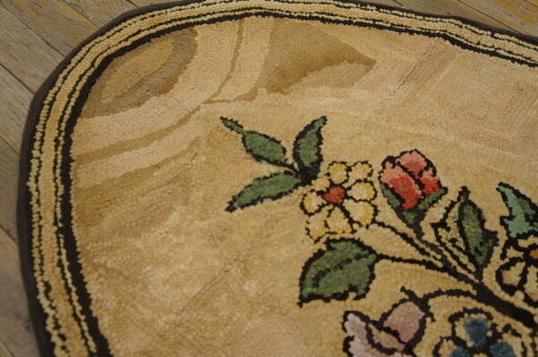 Detail of a tan hooked rug with a floral pattern of red, yellow, and green on rustic wood floor.