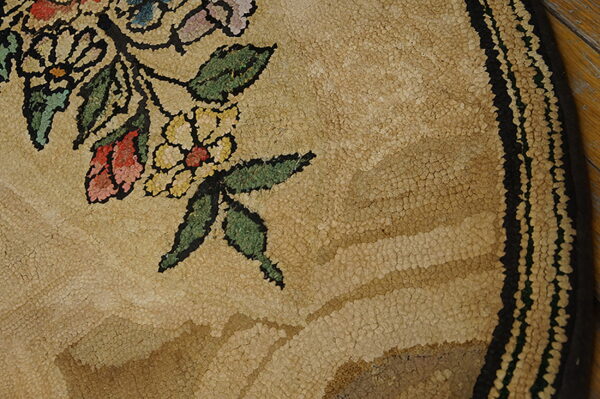 Textured tan rug detail with pink, yellow, and green floral motifs and a black striped outer border.