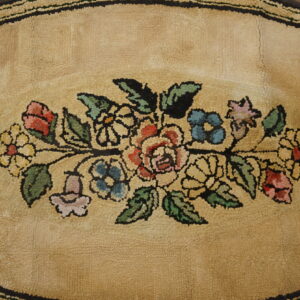 Tan hooked oval rug displays a vibrant floral garland bordered by dark brown stripes.