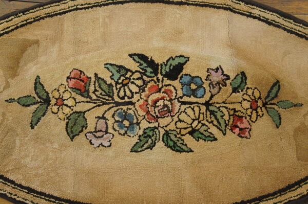 Tan hooked oval rug displays a vibrant floral garland bordered by dark brown stripes.