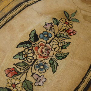 Oval beige looped-pile rug featuring a multicolored floral bouquet pattern on distressed wood flooring.