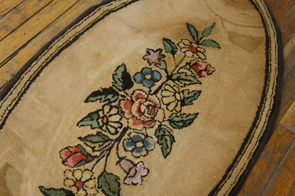 Oval beige looped-pile rug featuring a multicolored floral bouquet pattern on distressed wood flooring.