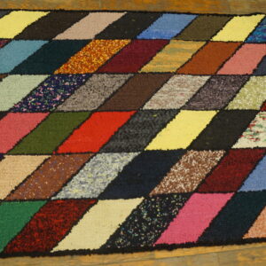 Textured multicolored rug with a geometric diamond pattern in many shades on wooden flooring.