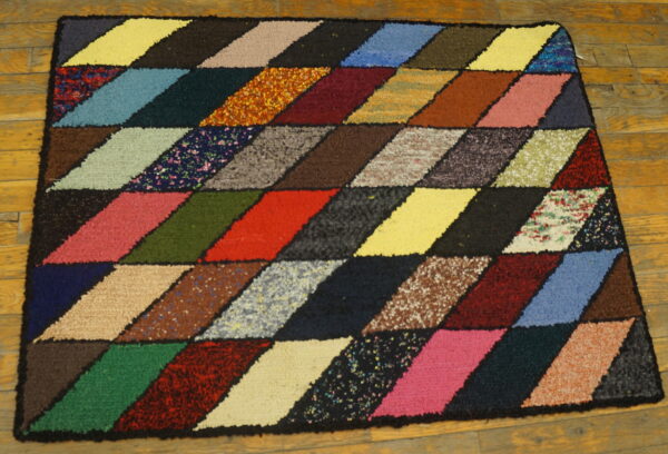 Textured multicolored rug with a geometric diamond pattern in many shades on wooden flooring.