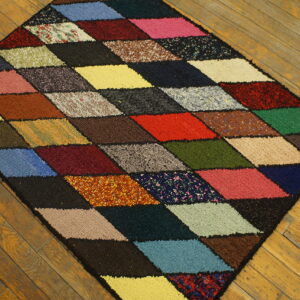 Textured, multicolored diamond-pattern rug sits diagonally on a rustic wooden plank floor.