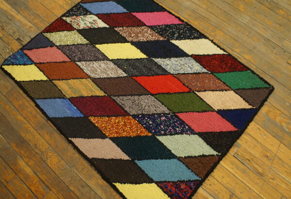 Textured, multicolored diamond-pattern rug sits diagonally on a rustic wooden plank floor.