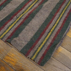 Low-pile gray rug with red, dark green, and yellow stripes rests on worn wooden planks.