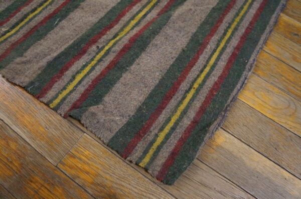 Low-pile gray rug with red, dark green, and yellow stripes rests on worn wooden planks.