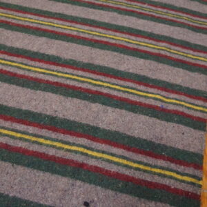 A gray, green, red, and yellow striped rug rests on worn, orange-toned wood flooring.