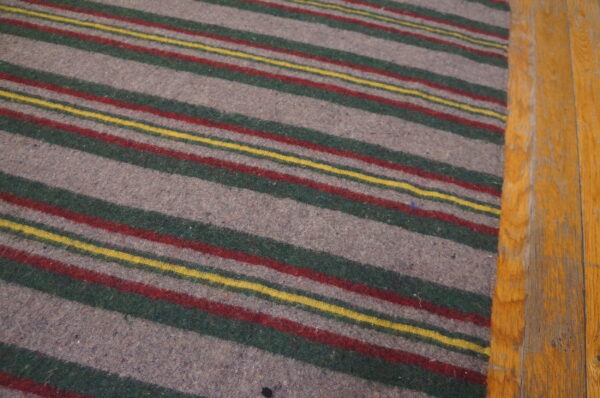 A gray, green, red, and yellow striped rug rests on worn, orange-toned wood flooring.