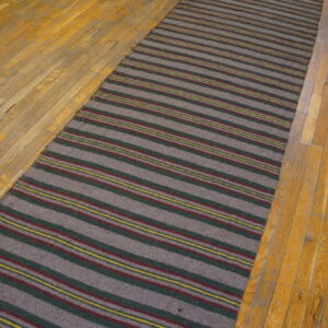 A gray striped runner rug with accent stripes of red, green, and yellow rests on aged hardwood flooring.