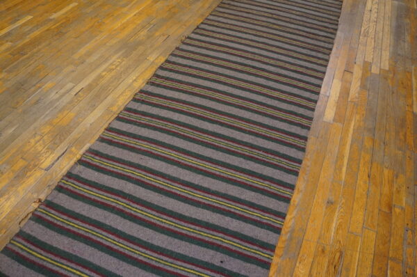 A gray striped runner rug with accent stripes of red, green, and yellow rests on aged hardwood flooring.