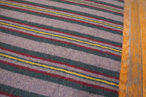 Low-pile gray rug featuring horizontal stripes of green, red, and yellow on wood flooring.