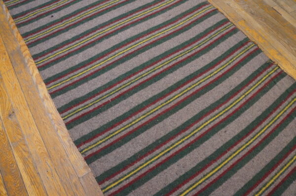Low-pile gray-brown rug features diagonal green, red, and thin yellow stripes on a light wood floor.
