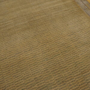 A textured tan rug with dark gray dash patterns lies diagonally on distressed hardwood flooring.