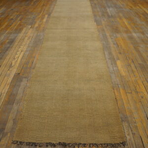 Low-pile golden-tan runner with woven blocks and fringe, centered on worn wood flooring.