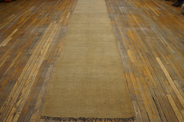 Low-pile golden-tan runner with woven blocks and fringe, centered on worn wood flooring.