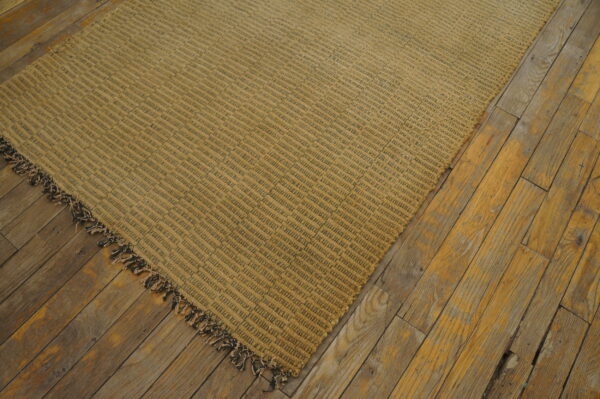 Textured tan and dark striped rug featuring fringe, displayed on weathered golden hardwood flooring.