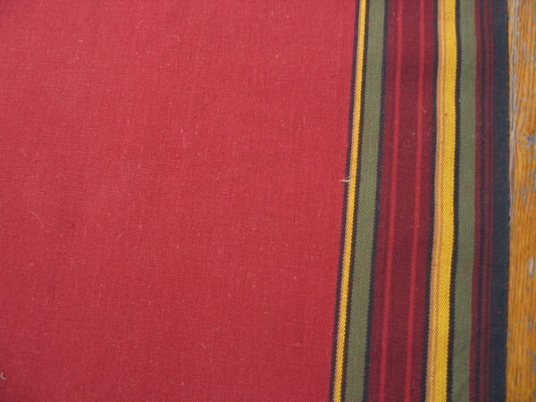 Red flatweave rug surface with a multicolored vertical stripe border next to worn brown wood.