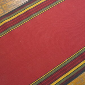A deep red flatweave rug runner with striped borders in yellow, olive, and burgundy on wood flooring.