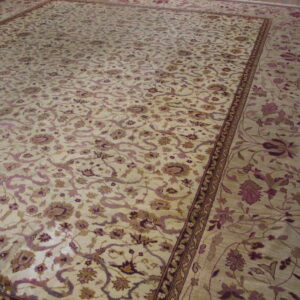 Cream rug with an elaborate traditional floral pattern in mauve and brown, displayed on a wood floor.