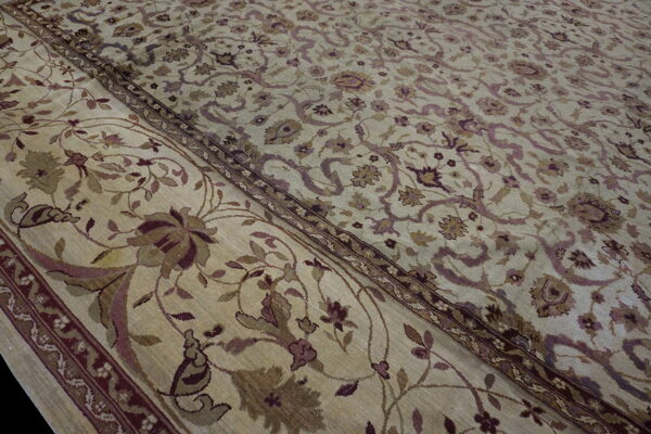 Close-up of a low-pile rug showing a tan field and border with muted purple and brown florals.