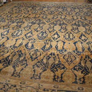 Oversized, low-pile rug in deep blue and gold with an intricate repeating medallion and stylized figural pattern.