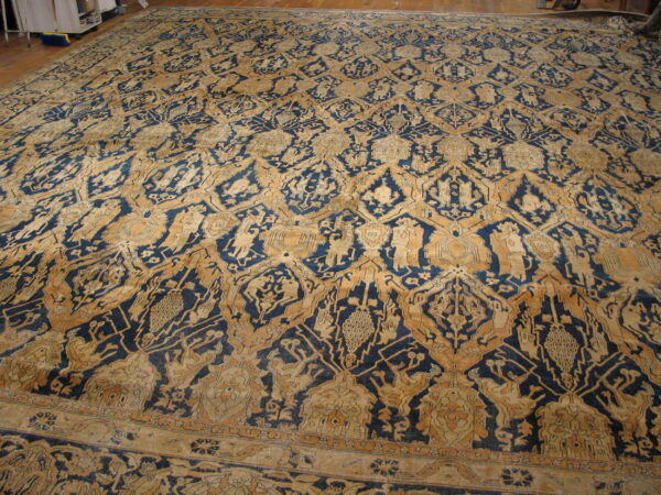 Oversized, low-pile rug in deep blue and gold with an intricate repeating medallion and stylized figural pattern.