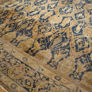 Low pile rug with complex traditional designs in faded navy and tan, partially resting on a wood floor.