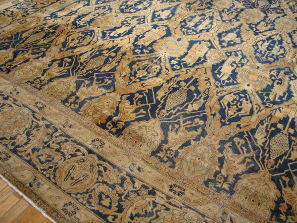 Low pile rug with complex traditional designs in faded navy and tan, partially resting on a wood floor.