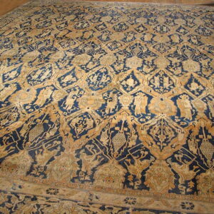 A large indigo and ochre rug displays a repetitive overall geometric pattern on wood flooring.