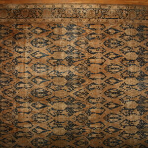 Large low-pile rug in dark blue and camel featuring a repeated abstract diamond pattern on wood planks.