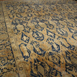 Intricate blue and gold traditional rug displaying stylized patterns and borders on wood flooring.