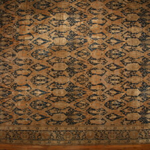 Ornate area rug with a dark blue and tan distressed repeating medallion pattern on wood flooring.