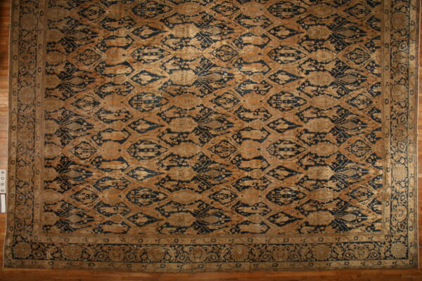 Ornate area rug with a dark blue and tan distressed repeating medallion pattern on wood flooring.
