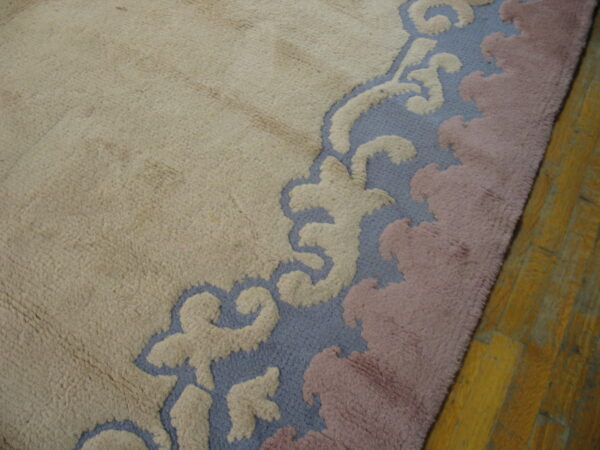 Textured, high-pile rug in beige with a sculpted blue, cream, and mauve scrolled border on wood planks.