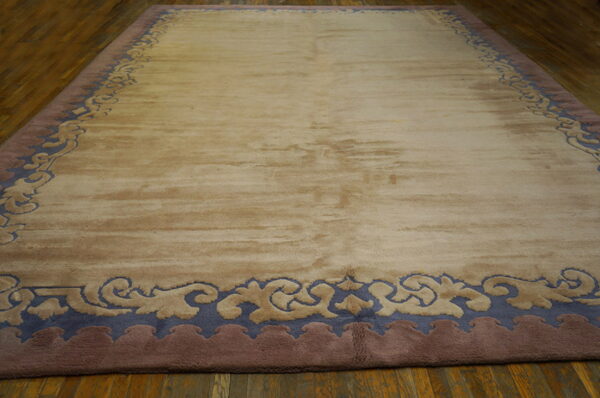 Large beige rug with a slate blue and mauve curvilinear border rests on a wooden floor.