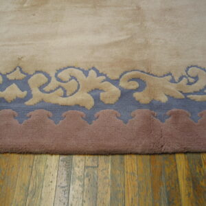High-pile rug edge featuring beige scrolling patterns on blue and mauve borders over a wood floor.