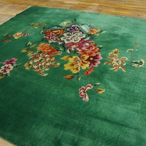 Lush green rug with a central cluster of yellow, magenta, and orange floral designs on hardwood.