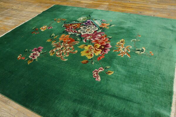 Lush green rug with a central cluster of yellow, magenta, and orange floral designs on hardwood.